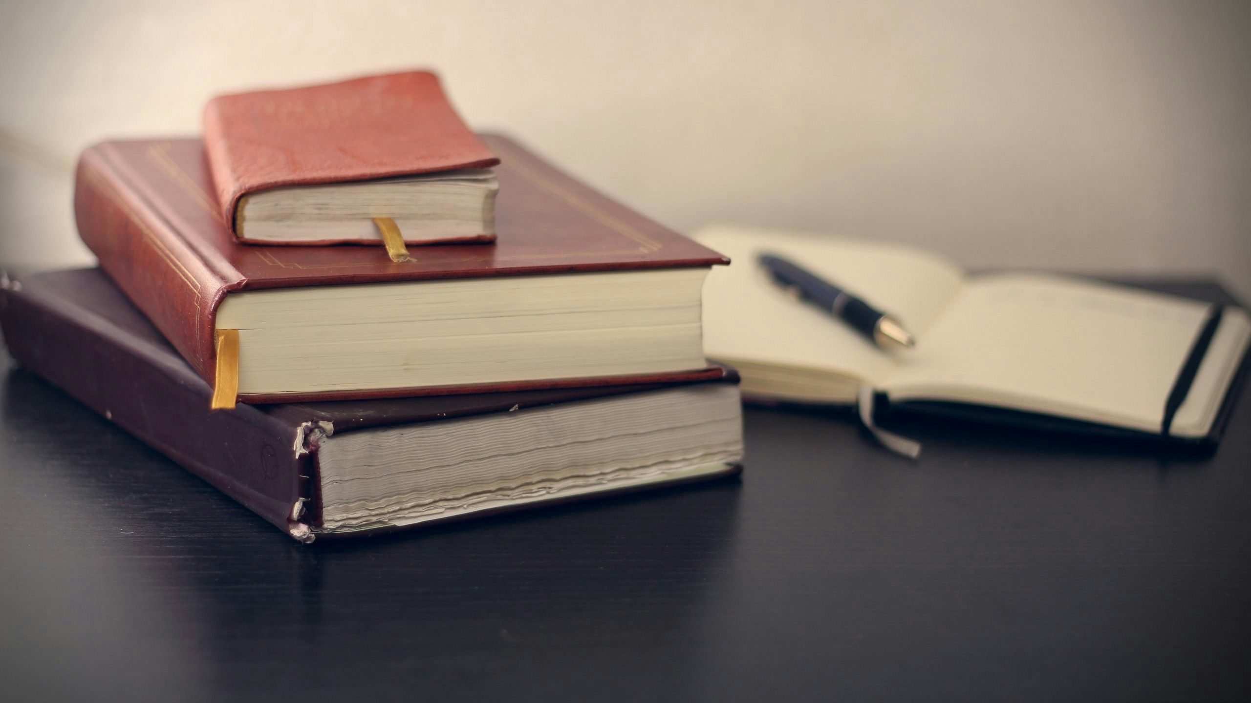 Three books stacked in front of an open notebook with a pen on top of it.